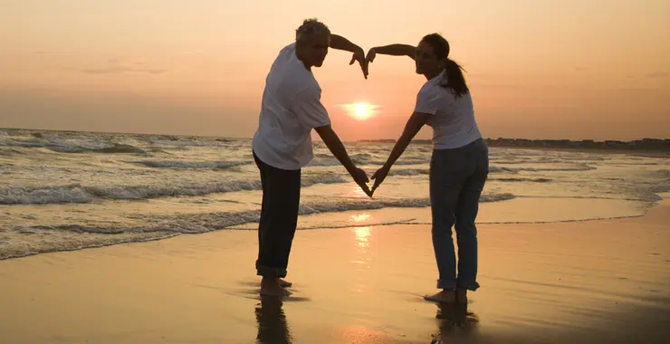 couple at sunset on beach with heart arms